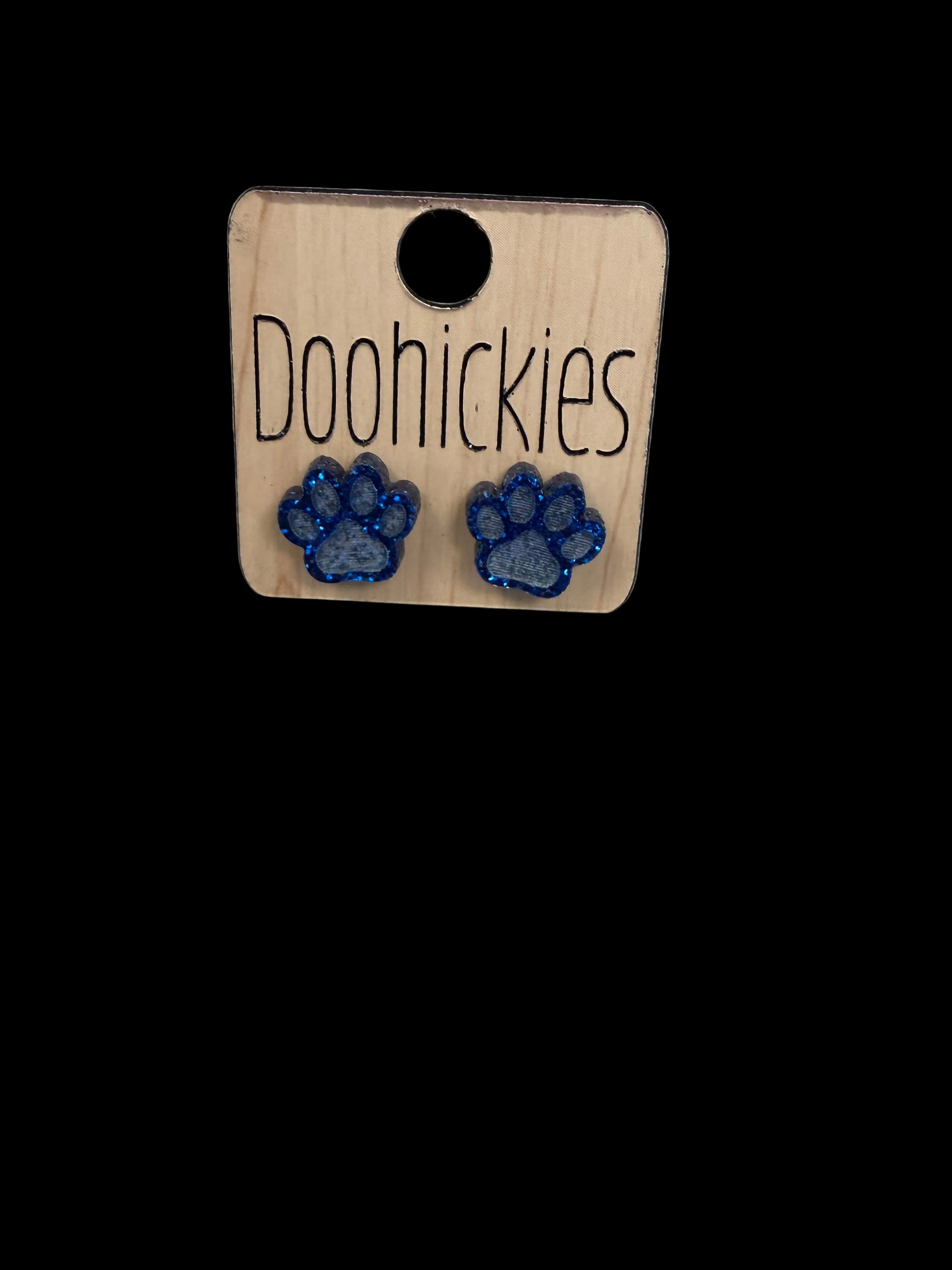 Wooden tag with 'Dood Hickies' branding and blue paw print designs on a concrete surface.