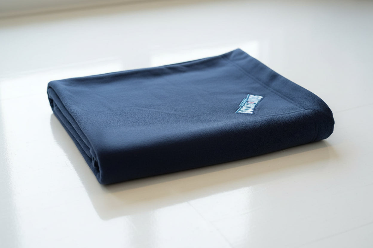 Person holding a folded navy blue garment with a visible brand logo in an indoor setting.